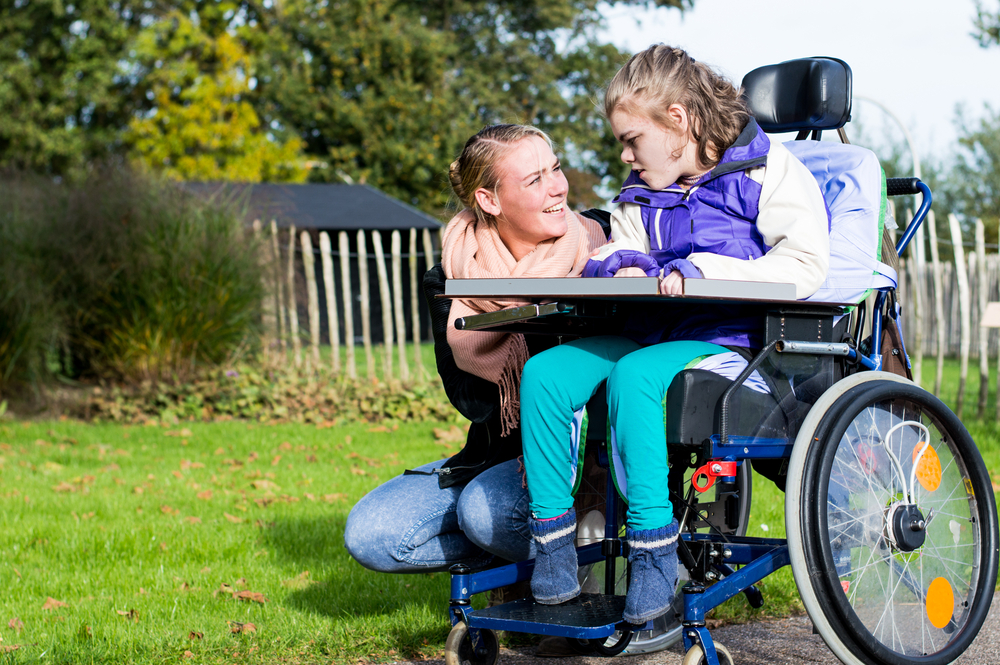 Disabled,Child,In,A,Wheelchair,Relaxing,Outside,With,A,Care